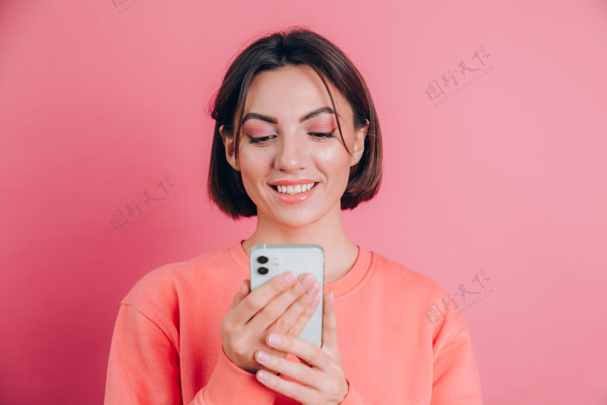 华丽可爱快乐的年轻漂亮的女人用手机在粉红色的墙壁背景上单独摆姿势女性年轻一个