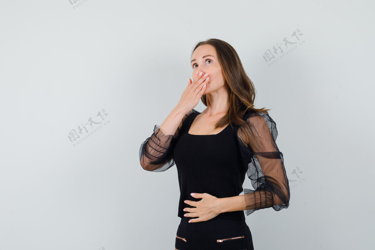 漂亮一只手捂着嘴 另一只手放在肚子上的年轻女子 穿着黑色上衣和黑色裤子 看上去很胆小前视图肚子女性衬衫