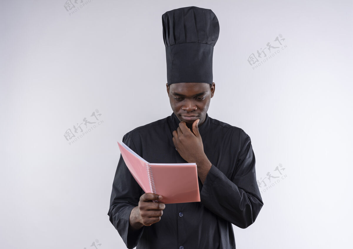 空间年轻体贴的非洲裔美国厨师穿着厨师制服 拿着并看着白色的笔记本和复印空间年轻制服复制