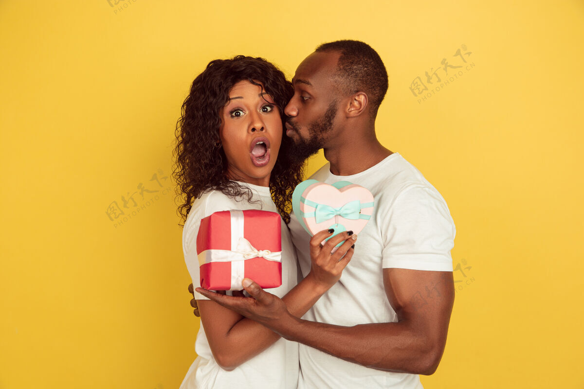 男朋友手持礼品盒情人节庆祝 快乐的非洲裔美国夫妇隔离在黄色的墙上人类情感的概念 面部表情 爱情 关系 浪漫的节日情人节面部立场