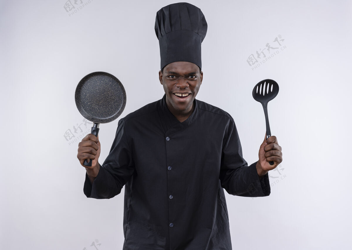 年轻穿着厨师制服的年轻的美国黑人厨师拿着平底锅和锅铲放在白色的地板上 上面留有复印空间抹刀制服平底锅