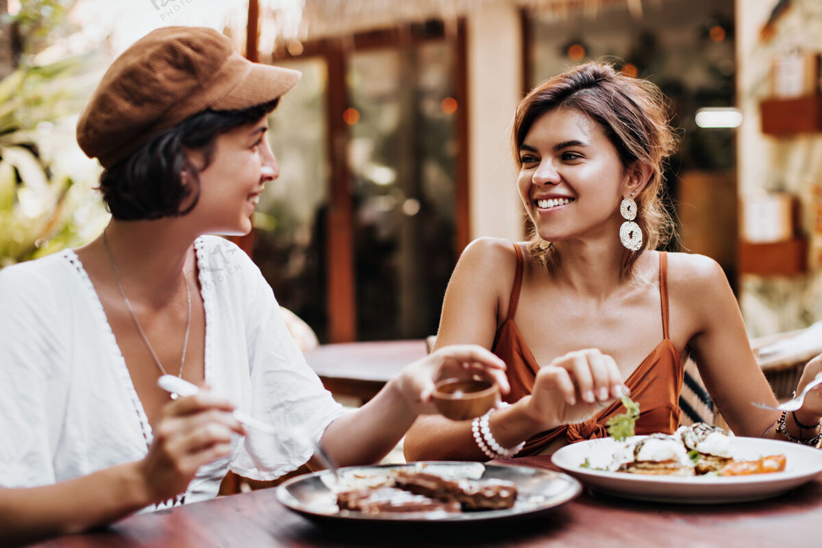 度假村迷人的棕褐色女人在街上咖啡馆吃着美味的食物 心情很好朋友人热
