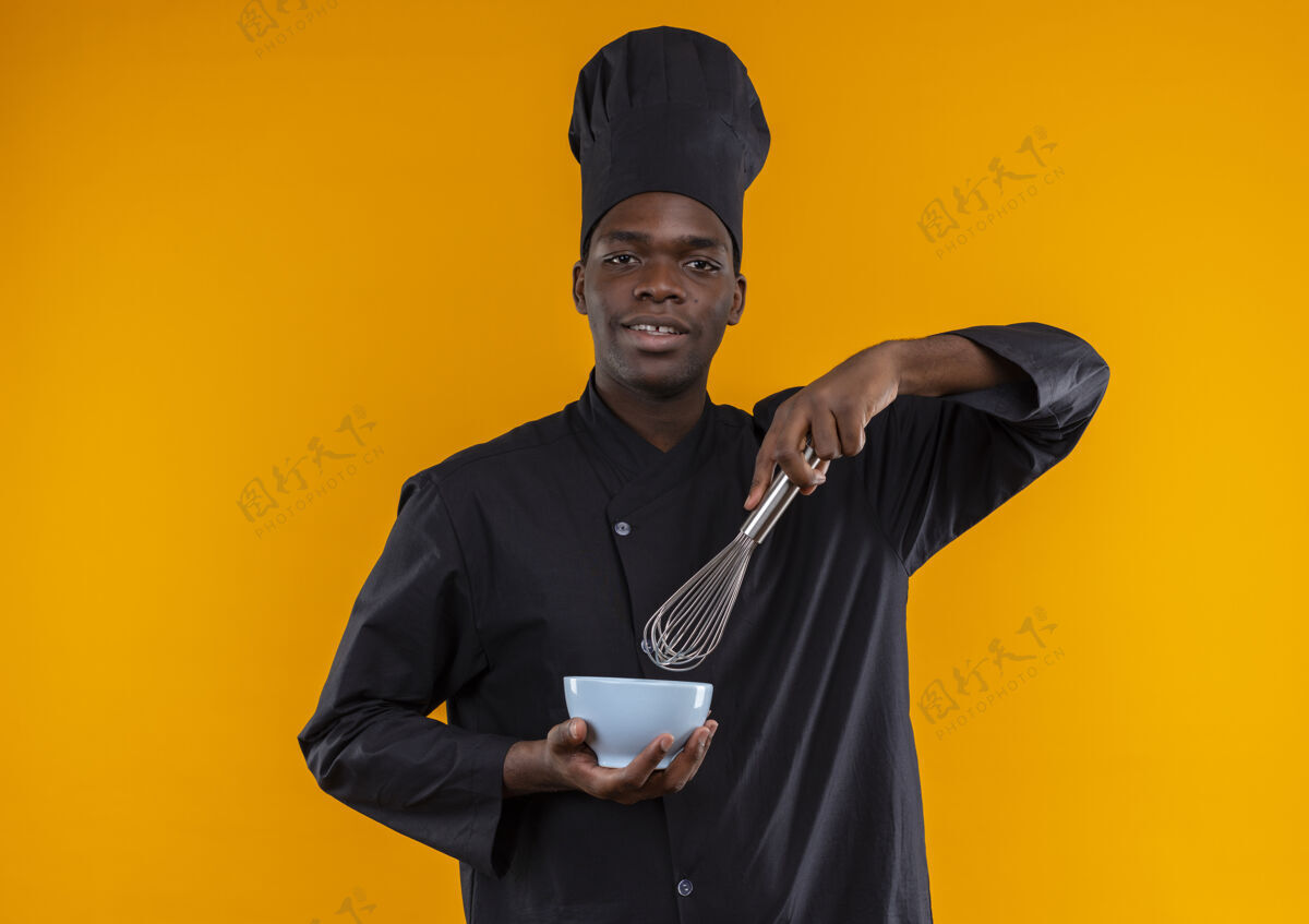 空间身着厨师制服的年轻美籍黑人厨师拿着搅拌器和碗 看着橙色的相机 留着复印空间烹饪厨师复制