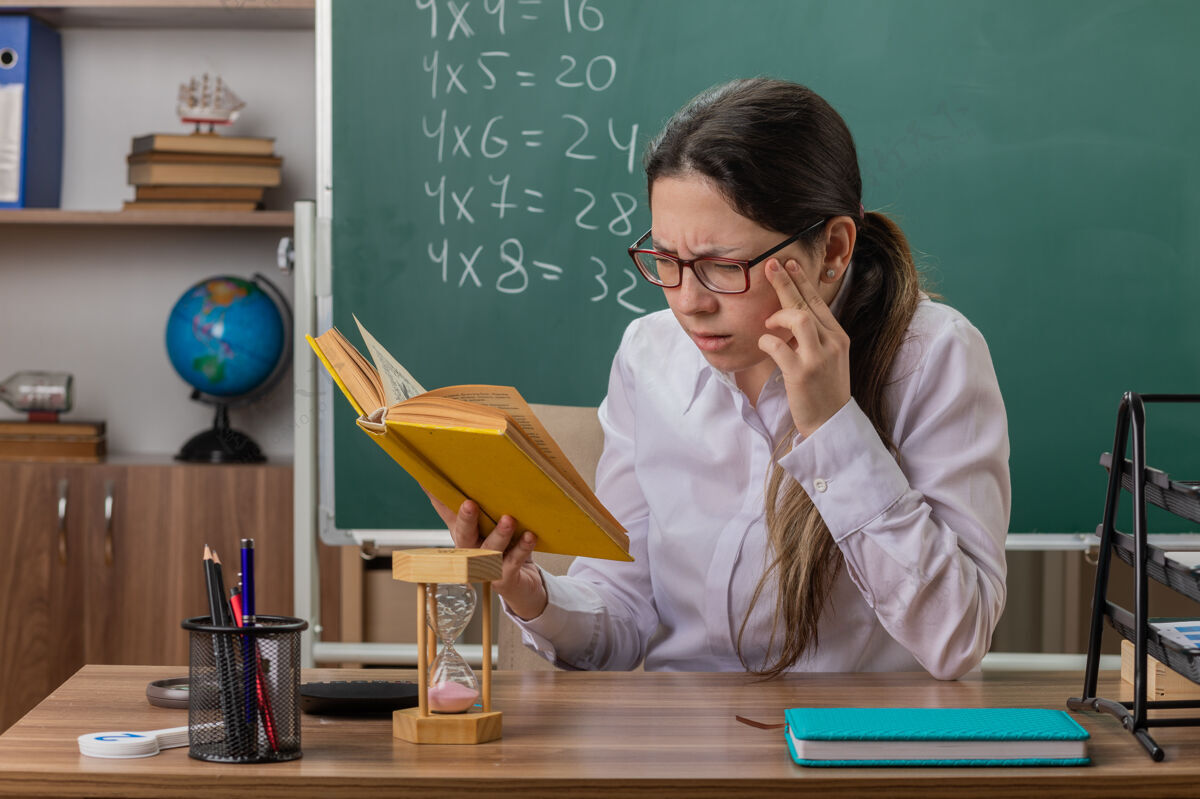 女人年轻的女老师戴着眼镜拿着备课的书看得很困惑课老师年轻