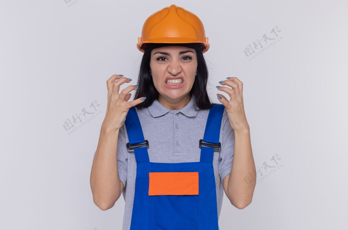建筑工人愤怒的年轻建筑妇女穿着建筑制服 戴着安全帽 高举双臂大喊大叫站立年轻举起
