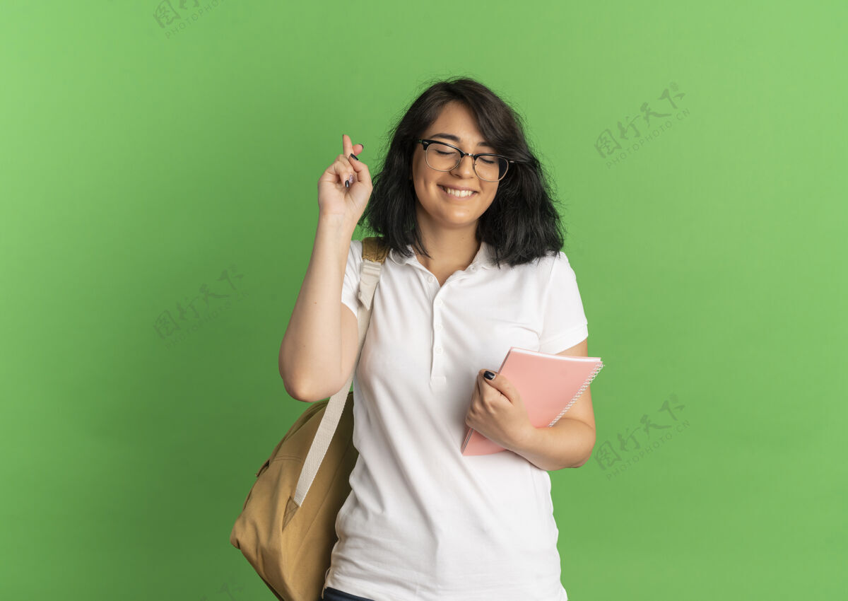 眼镜年轻漂亮的高加索女生戴着眼镜 背着书包 拿着笔记本在绿色的草地上点了点 留着复印空间包女学生笔记本