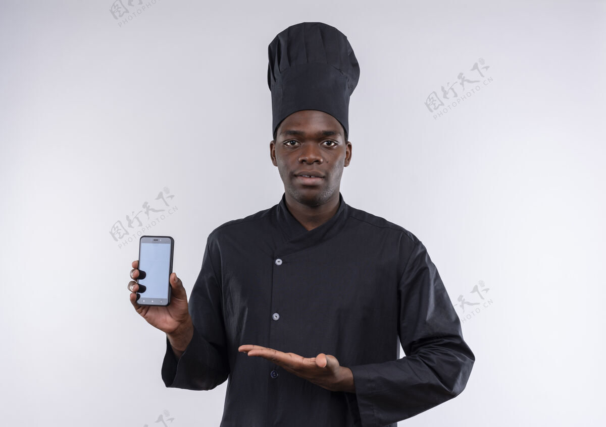 复制身着厨师制服的年轻自信的美国黑人厨师拿着并指着白色的手机 留着复印空间空间点制服