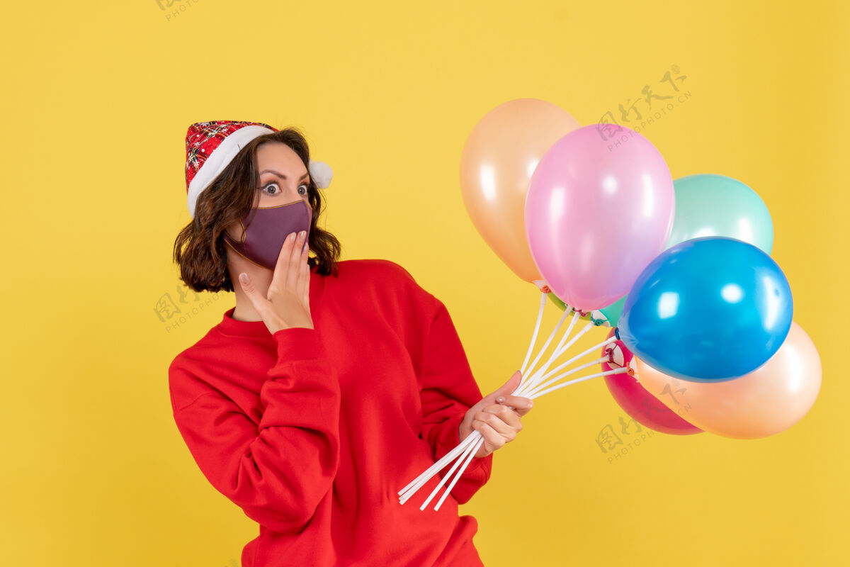 颜色正面图：戴着黄色面具手持气球的年轻女子外科口罩年轻女人派对
