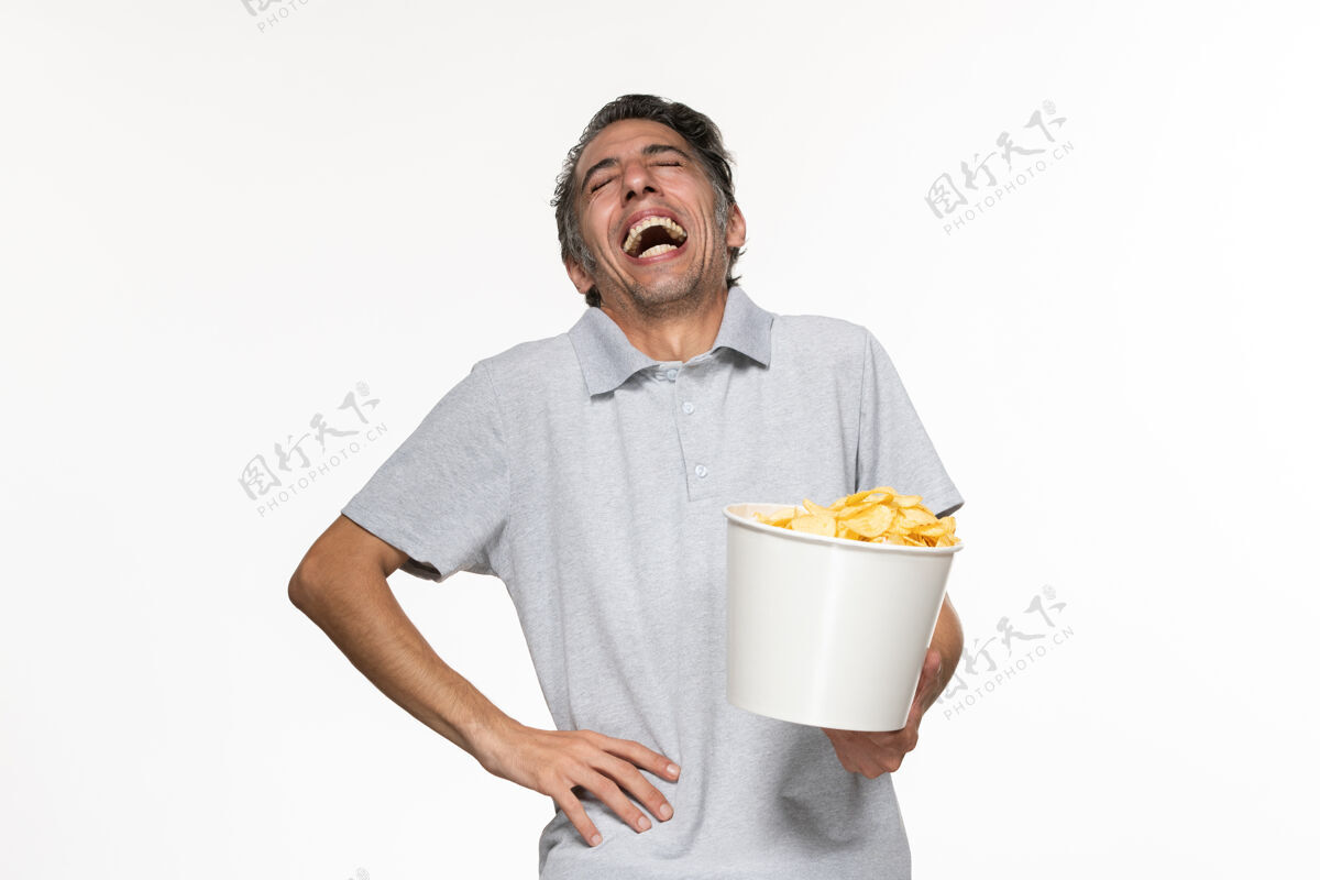 男正面图年轻的男性在吃薯片 在白色的表面上笑土豆电影院服务员