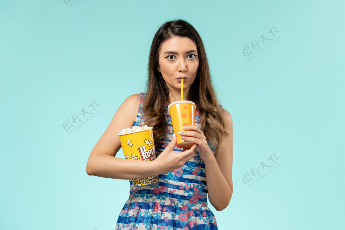 女正面图年轻女子拿着爆米花在蓝色的水面上喝酒电影电影剧院