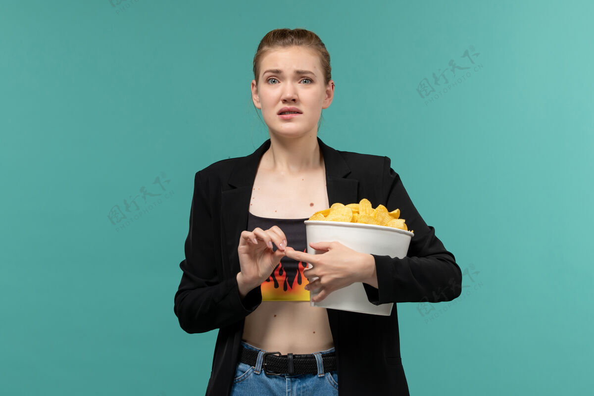 托盘正面图：年轻女性拿着薯片包 在浅蓝色的表面上看电影漂亮电影院包装