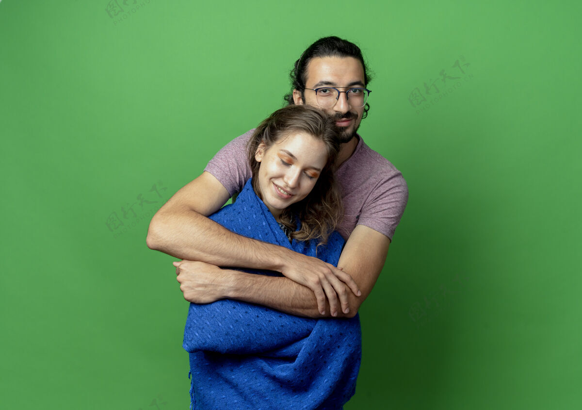 男人一对年轻的男女 热恋中的快乐 汉森的男人抱着他心爱的女朋友站在绿色的墙上毯子拥抱站着