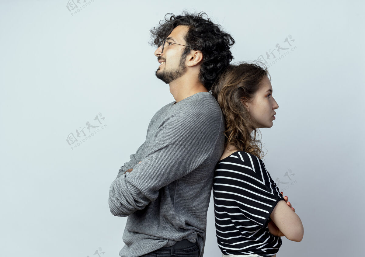 女人一对年轻夫妇背靠背地站在白墙上年轻人站起来夫妇