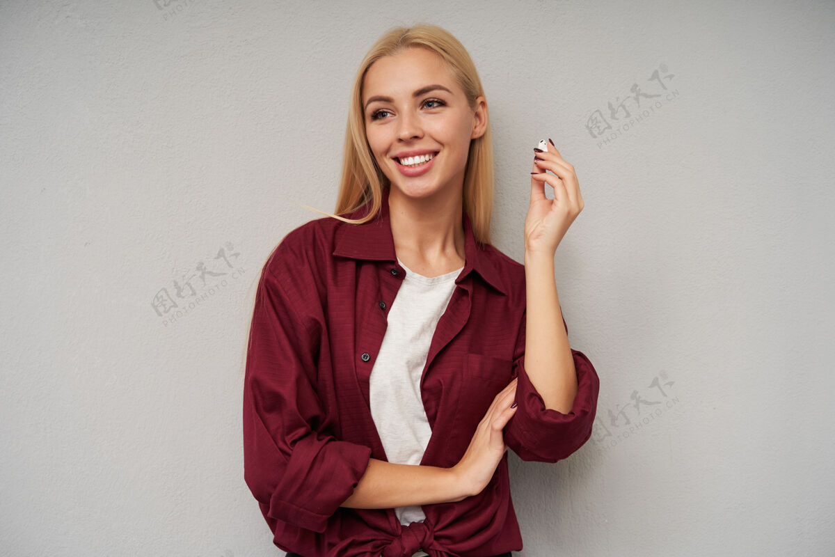 牙齿正面的年轻金发女性的肖像 随意的发型 拿出耳机 面带迷人的笑容 在浅灰色的背景下孤立地看着一边年轻人衬衫耳机