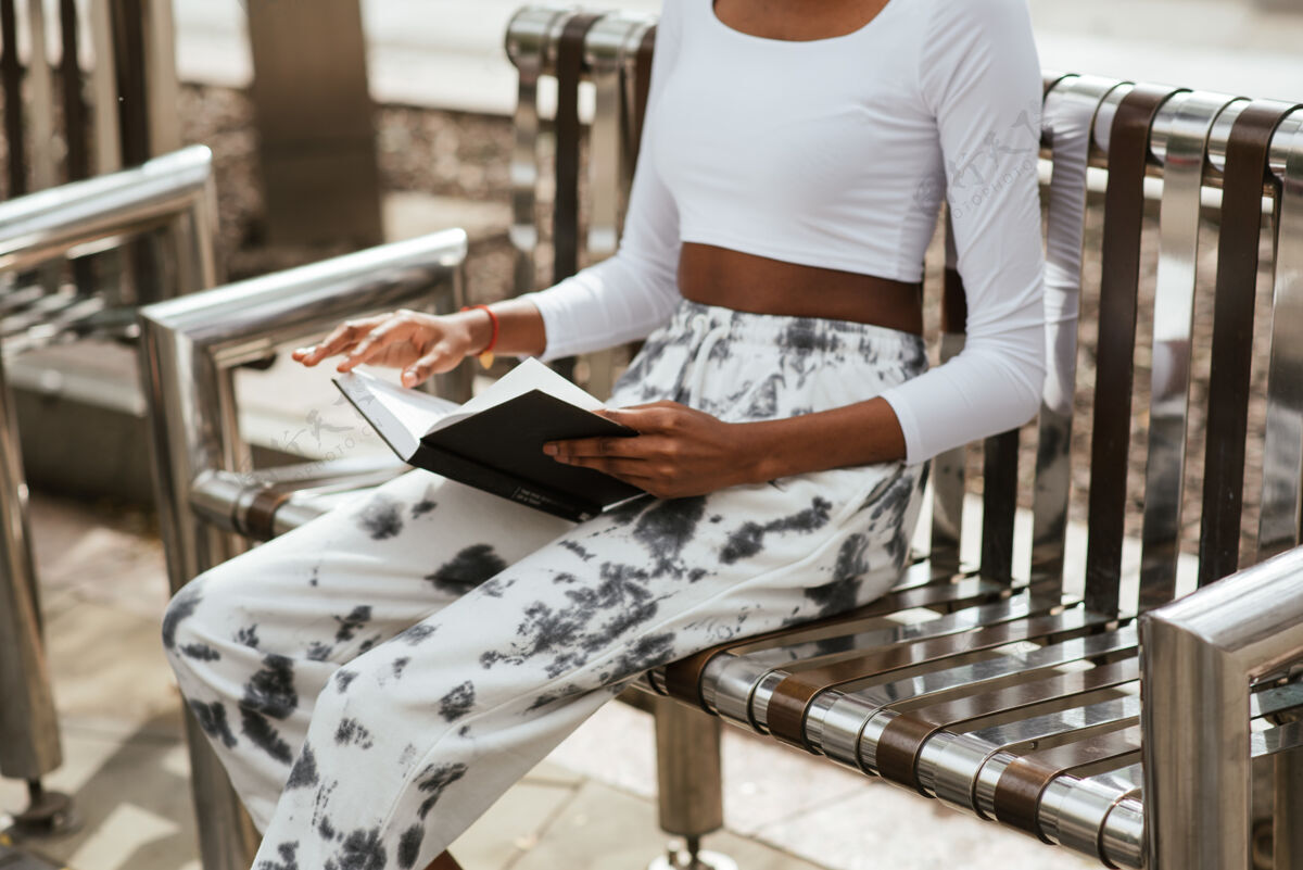年轻坐在长椅上看书的非裔美国女人微笑读书学习