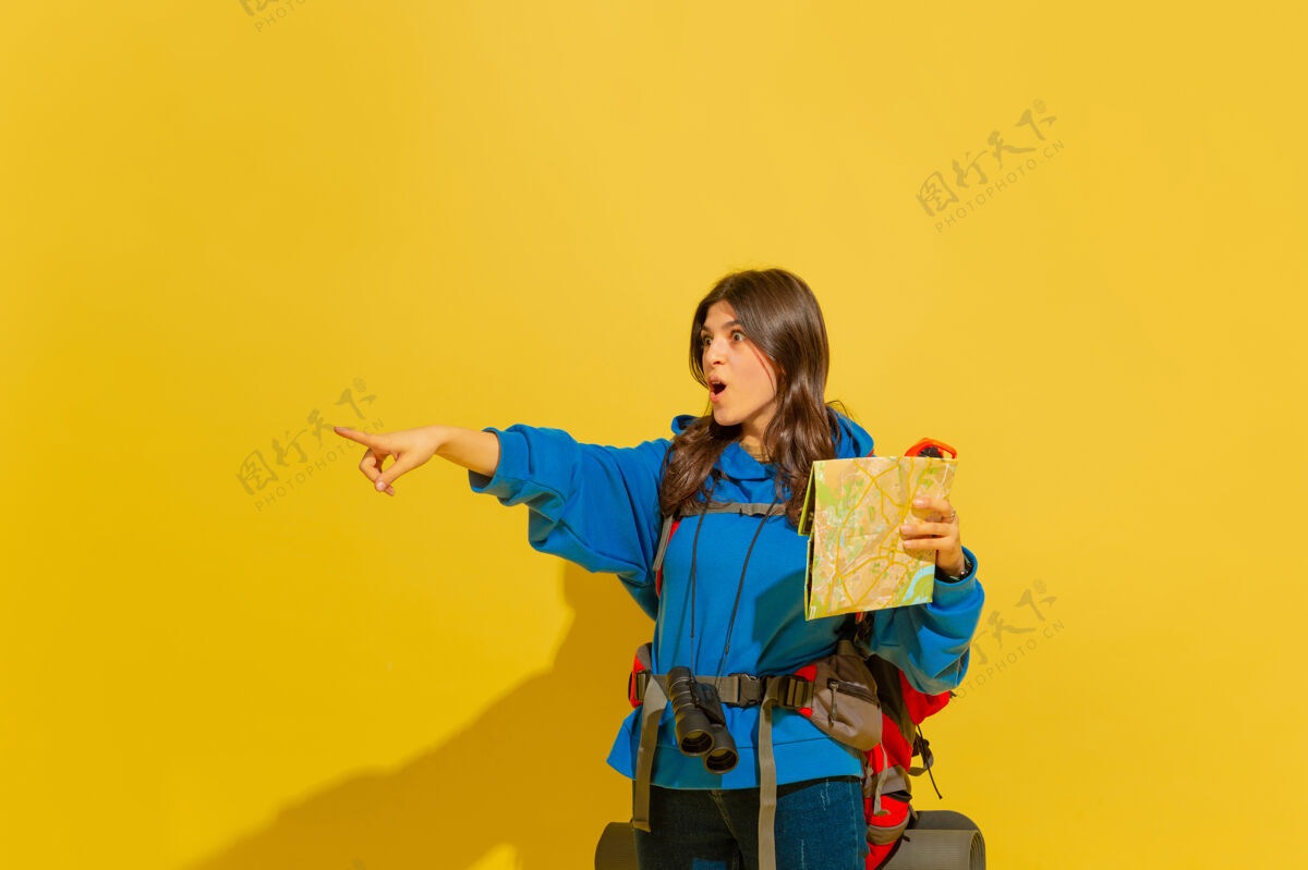 女人黄色摄影棚墙上 一个带着包和望远镜的快乐的年轻旅游女孩的画像手势旅游者手提箱