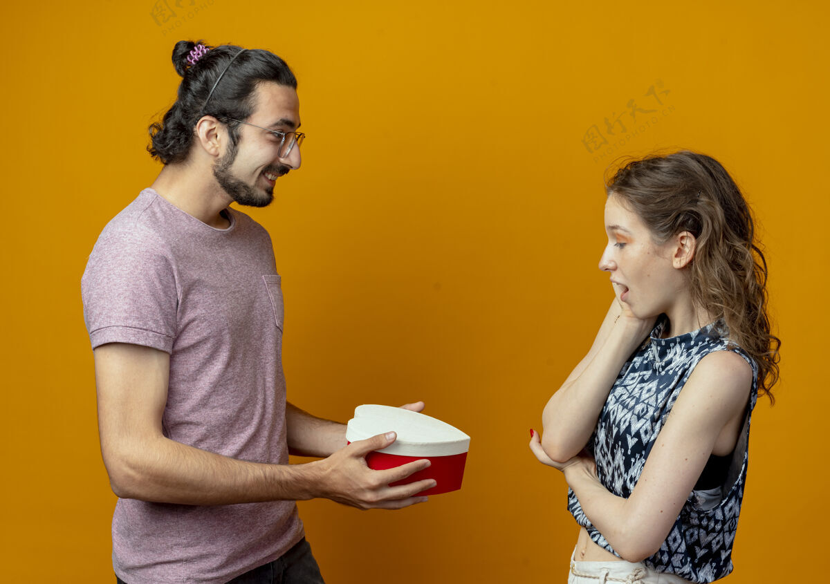 夫妻男人在橘色的墙上把礼物盒送给他那对年轻漂亮的姑娘们奉献女人年轻人