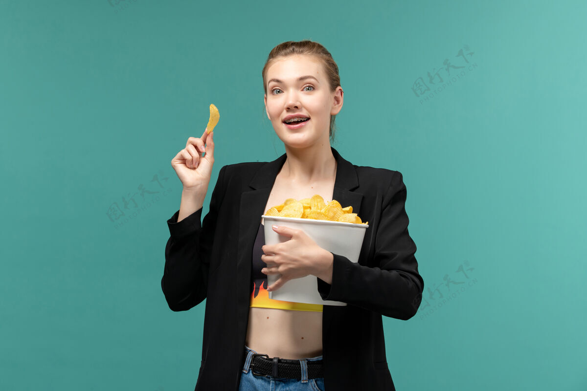 男正面图：年轻的女性拿着薯片 吃着薯片 在蓝色的水面上看电影电影秘书电影
