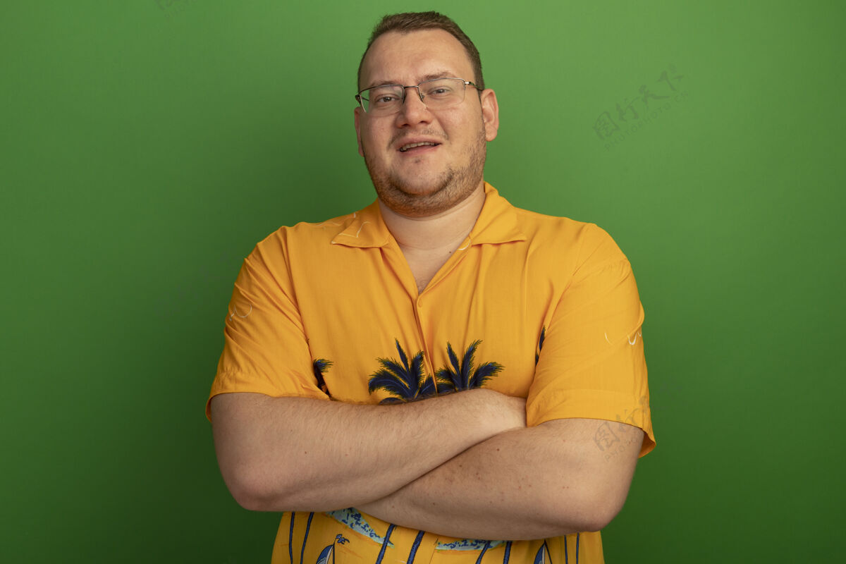 交叉一个戴着眼镜 穿着橙色衬衫 脸上挂着微笑 双臂交叉的男人站在绿色的墙上脸眼镜微笑