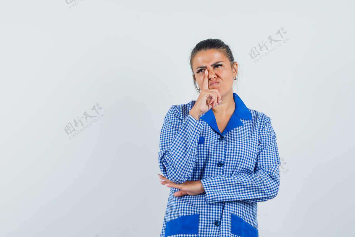 衬衫年轻女子站在思考的姿势 把食指靠近鼻子在蓝色方格睡衣衬衫和期待沉思前视图站着女性目录