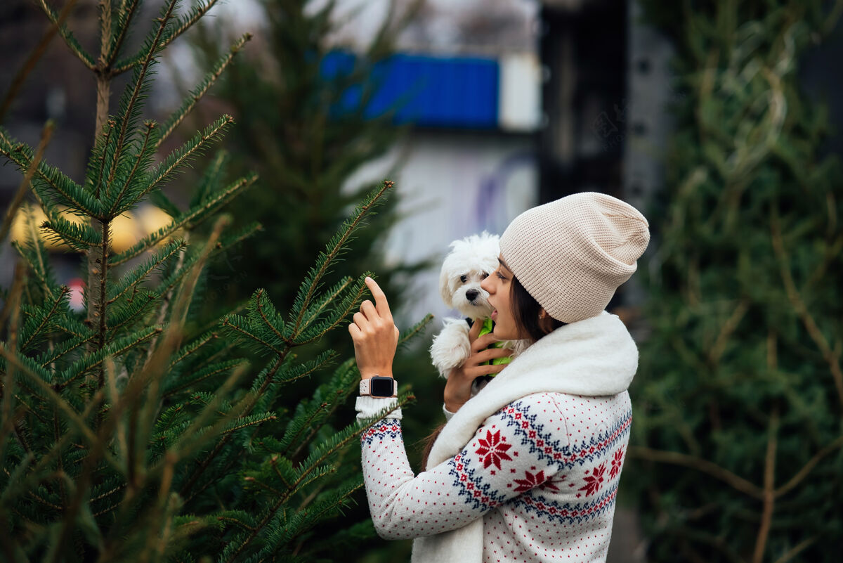 动物市场上一棵绿色的圣诞树旁 一个抱着一只白色狗的女人圣诞树可爱在一起