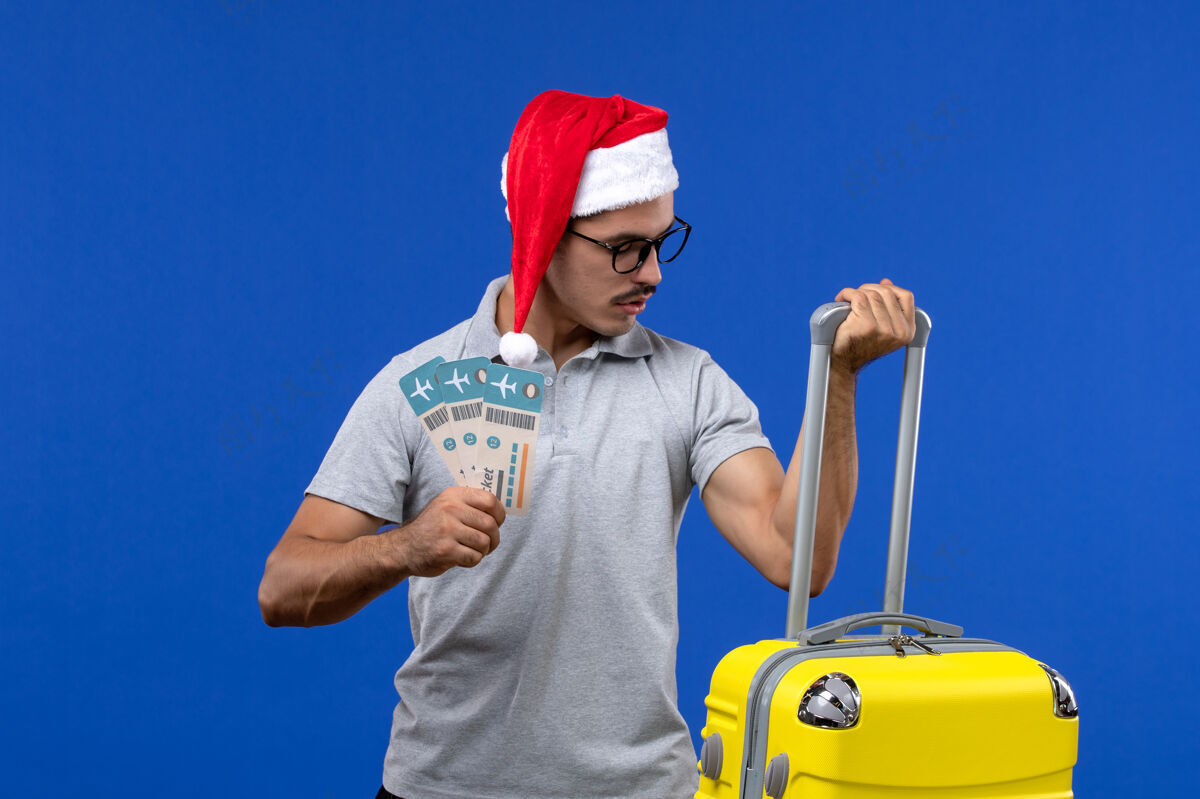 男人正面图：年轻男子提着沉重的袋子 拿着蓝墙航班度假飞机的机票携带视图工作