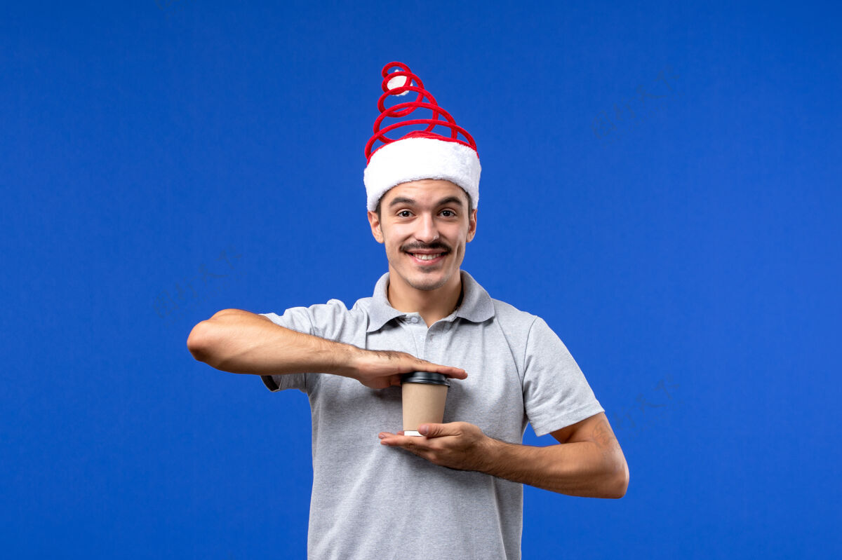 塑料正面图年轻男子手持塑料咖啡杯在蓝色墙壁上过年男子节日成人圣诞节咖啡