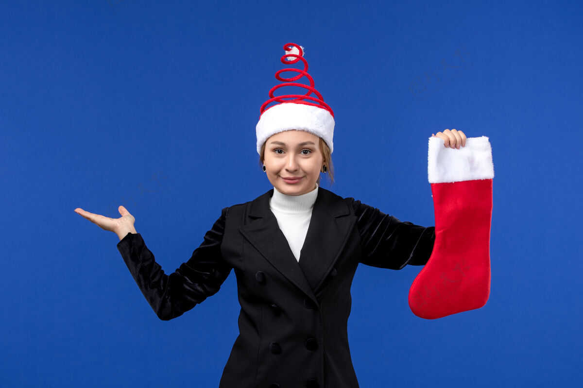 职业正面图：年轻女子手持红色圣诞袜在蓝色墙壁上过年人袜子前面