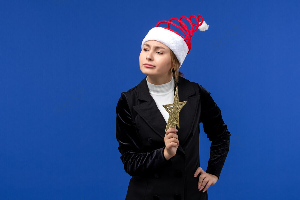 前面正面图年轻女性手持蓝色墙壁上的星形装饰新年假期圣诞节形状明星西装