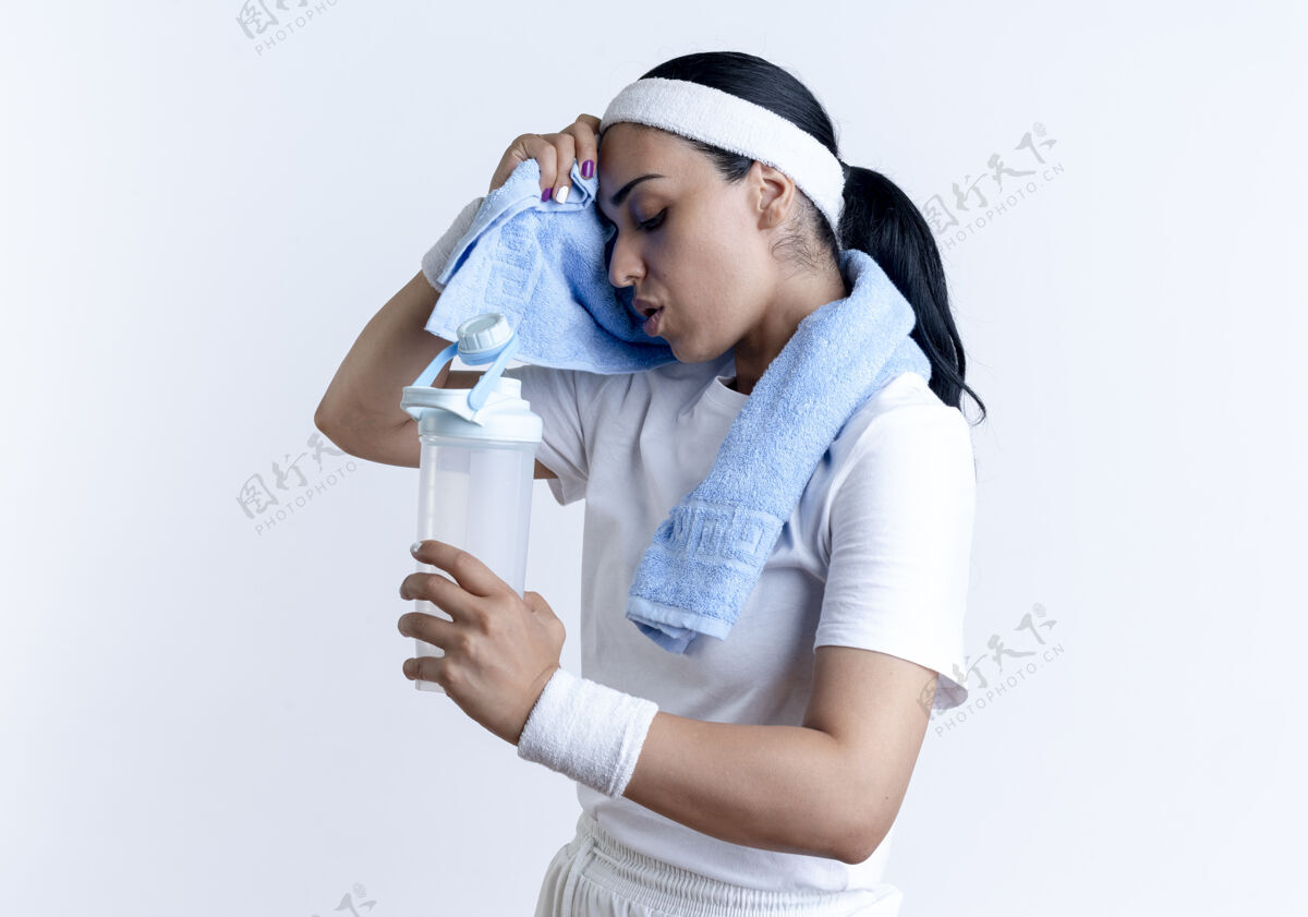 毛巾年轻疲惫的白人运动女性戴着头带和腕带站在一边 用毛巾擦拭额头拿着水瓶隔离在白色空间与复制空间复制空间运动