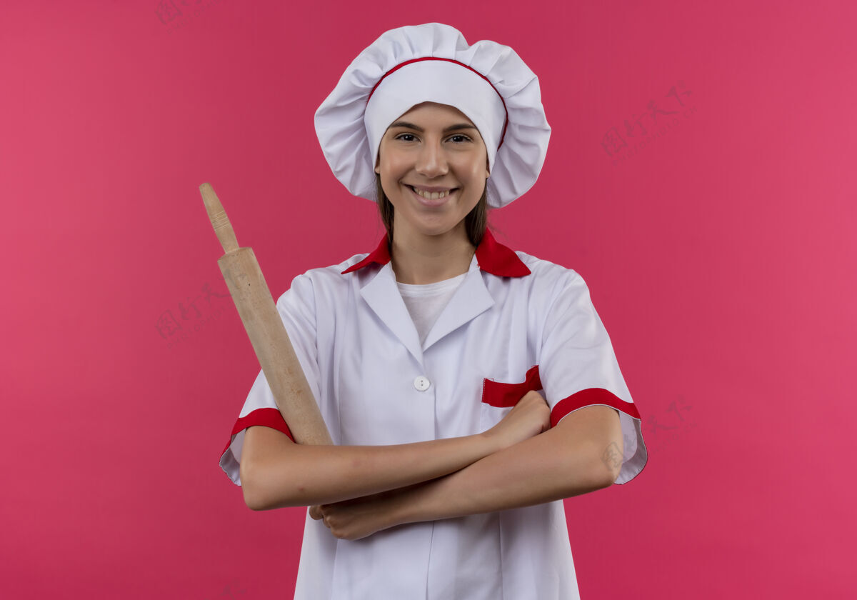 滚动身着厨师制服 面带微笑的白人厨师女孩手拿擀面杖 双臂交叉 在粉色空间与复印空间隔离开来空间粉红微笑