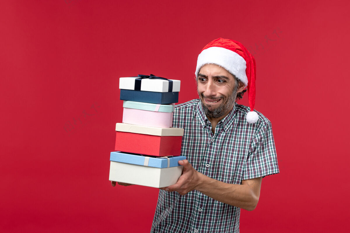 男性正面图：年轻男性手持新年礼物站在红桌子上帽子男人圣诞