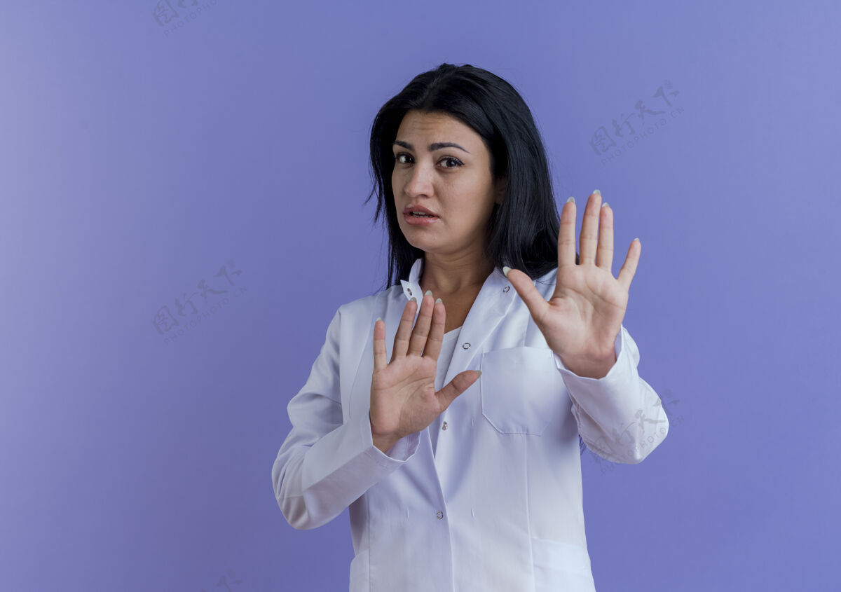 女性未出租的年轻女医生穿着医疗袍做没有手势孤立在紫色的墙上与复制空间手势表情不愉快
