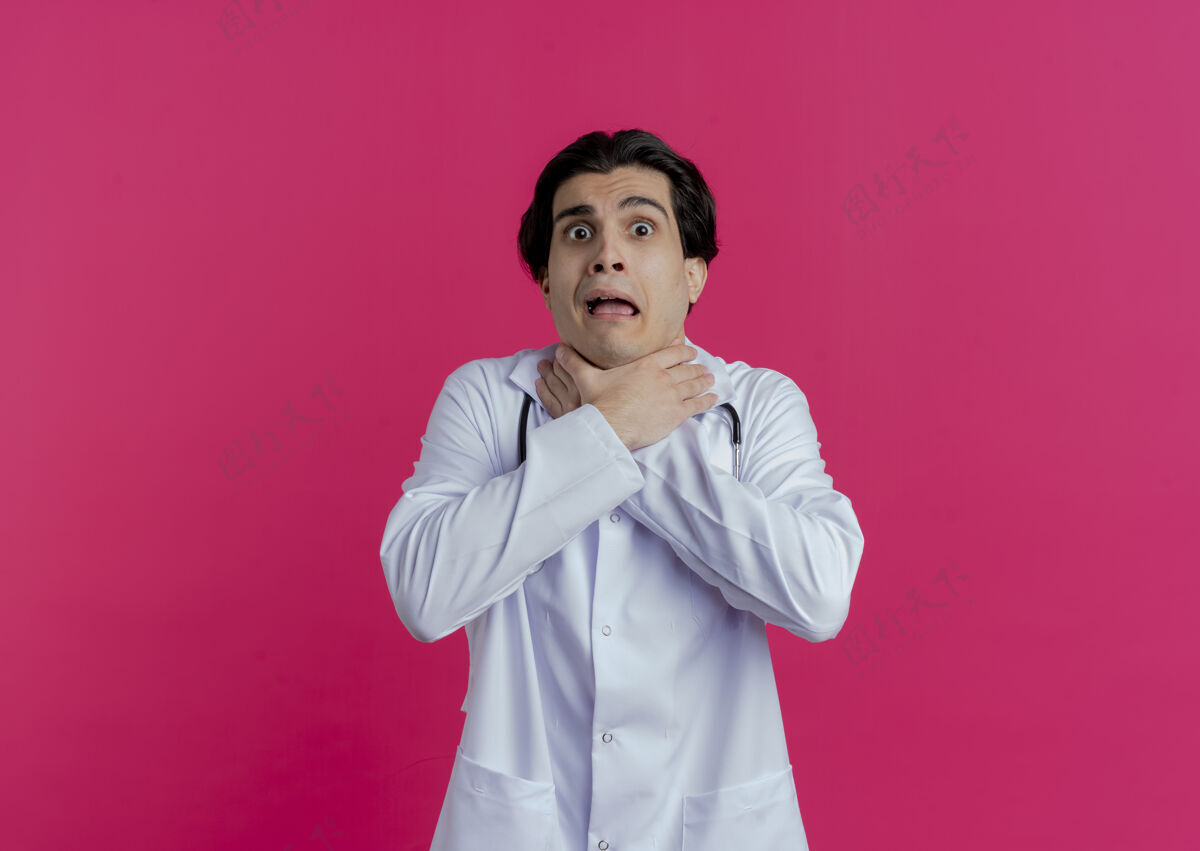 听诊器厌倦了年轻的男医生穿着医用长袍和听诊器窒息自己隔离在粉红色的墙上与复制空间医疗男性看