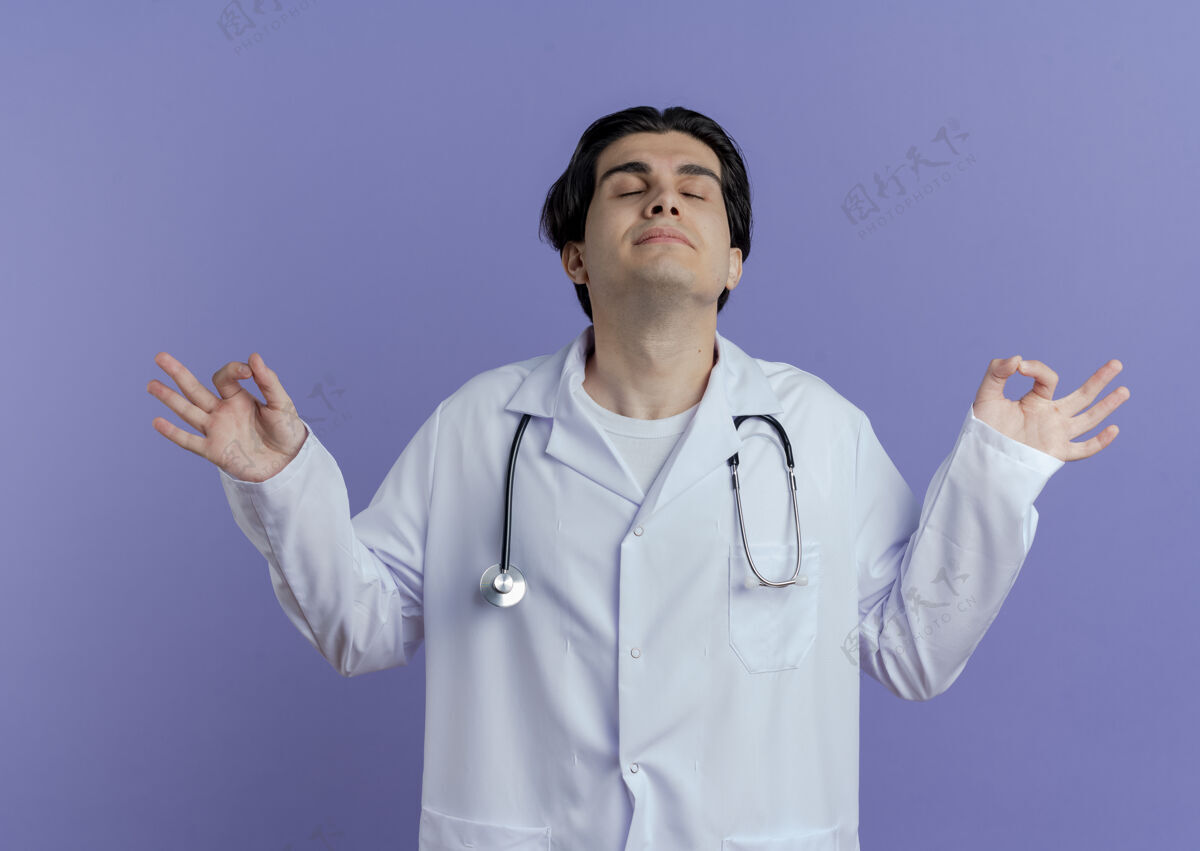 医生安静的年轻男医生 穿着医用长袍 戴着听诊器 闭眼在紫色的墙上封闭穿着和平