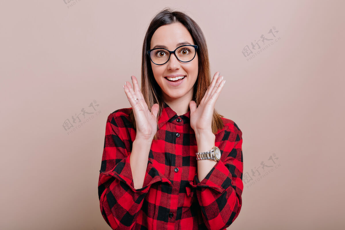 青少年画像中迷人的年轻女子身着衬衫 戴着眼镜 带着惊讶的情绪 在孤零零的墙上举手 真实的情感爱情积极肖像