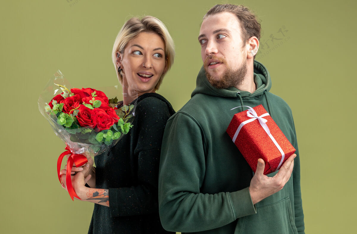 站一对穿着休闲服的年轻夫妇 带着礼物的快乐男人和带着鲜花的女人 背靠背地站在绿色的背景上庆祝情人节回来男人花