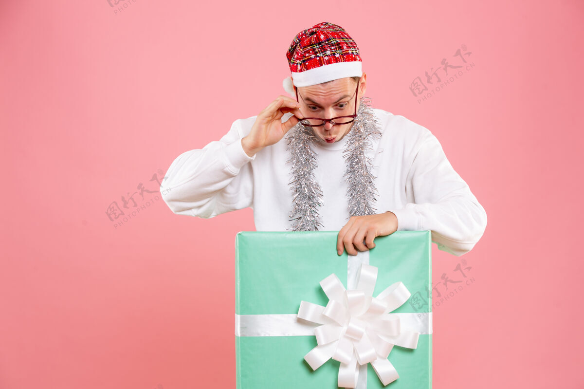圣诞节正面图：年轻男性在粉色背景上佩戴花环礼物肖像正面