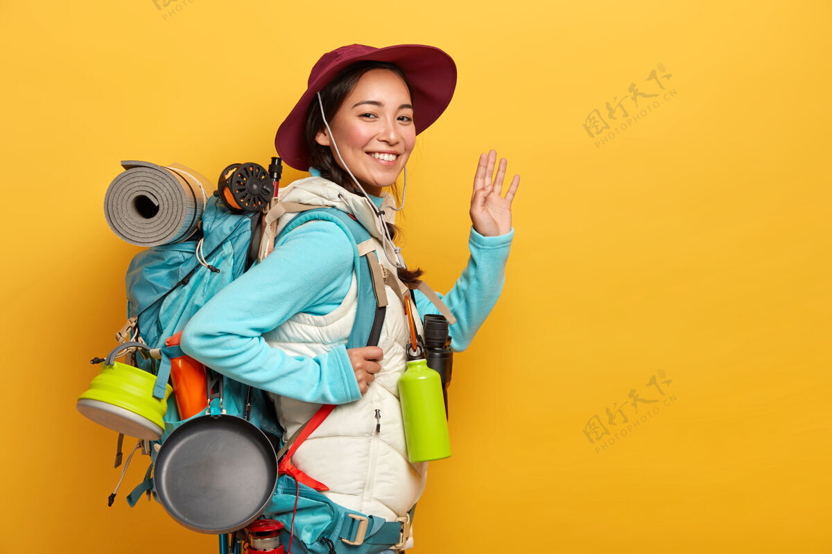 背包满脸笑容的亚洲女人背包有着欢快的表情 对着镜头挥舞着手掌 把所有必要的东西都装在大背包里游客室内包