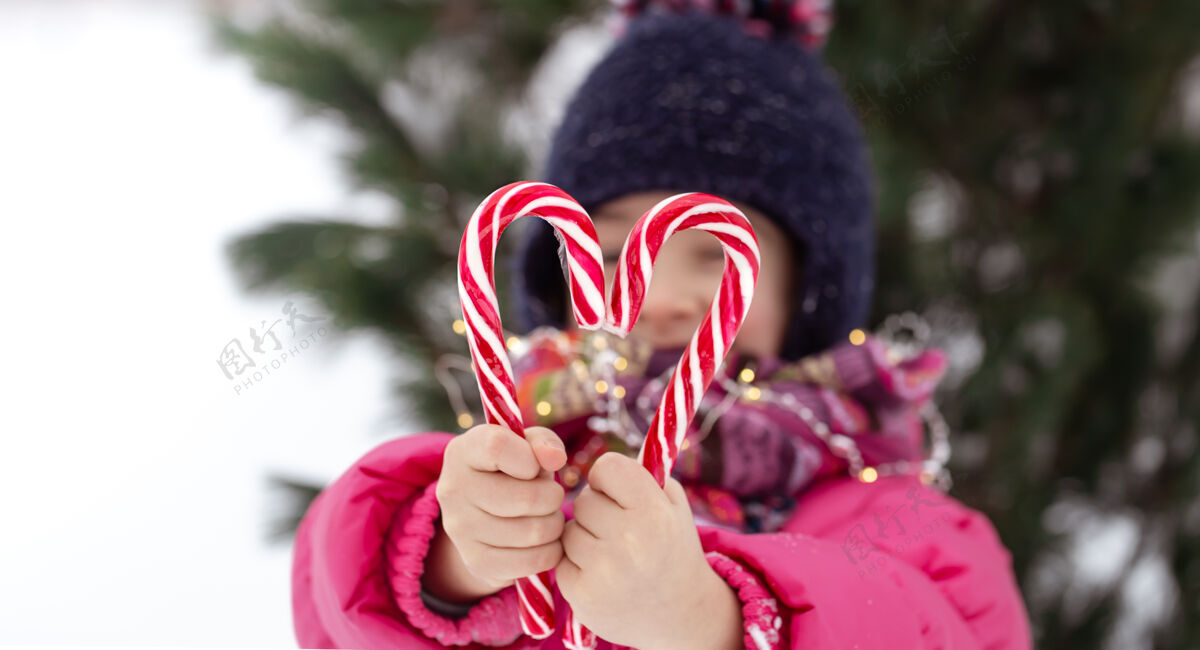 圣诞节带着一个大糖果棒的孩子在模糊的背景下寒假的概念手杖女孩雪