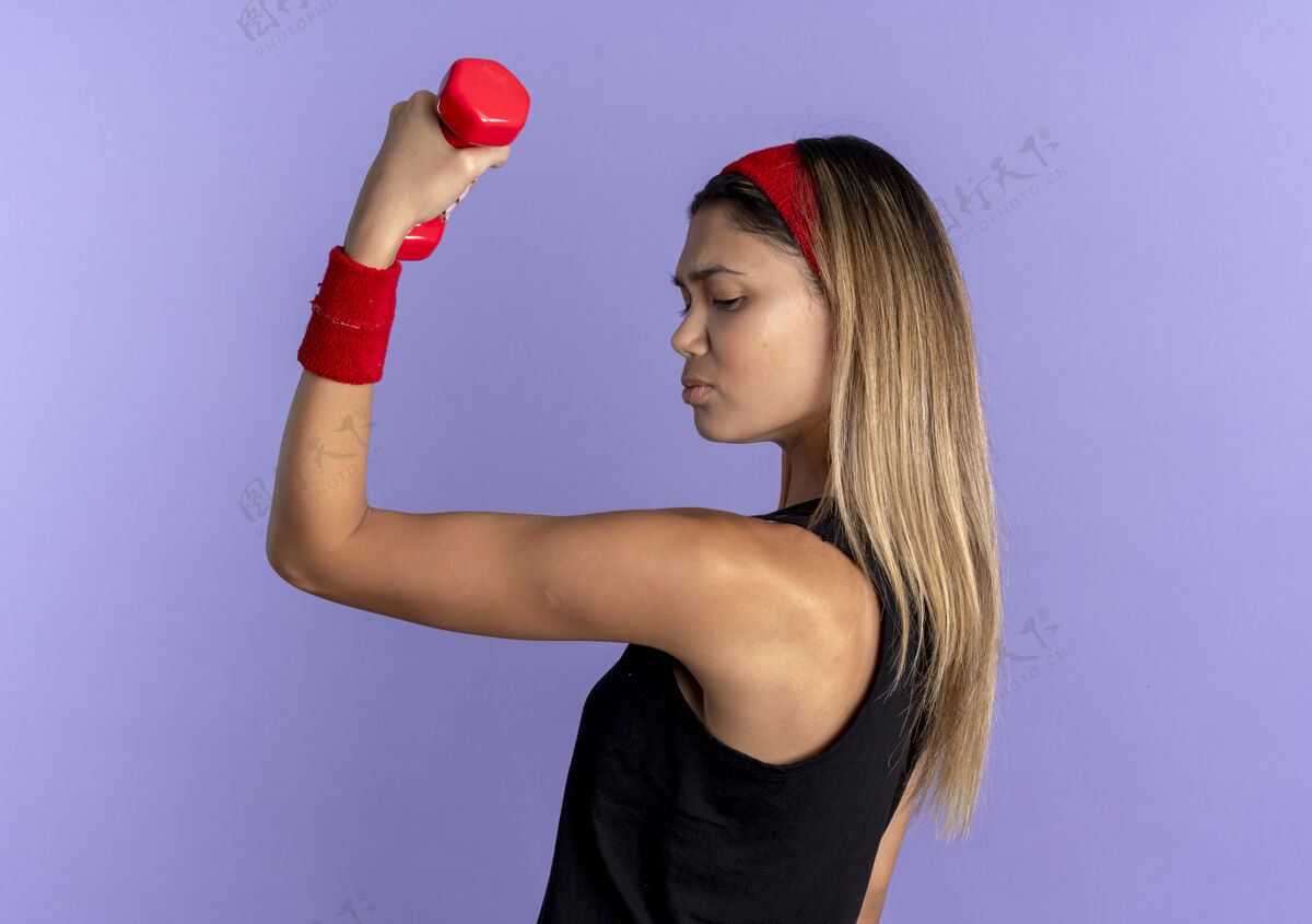 红色身穿黑色运动服 头戴红色头带的年轻健身女孩练习哑铃 展示的二头肌看起来比蓝色更自信哑铃年轻工作