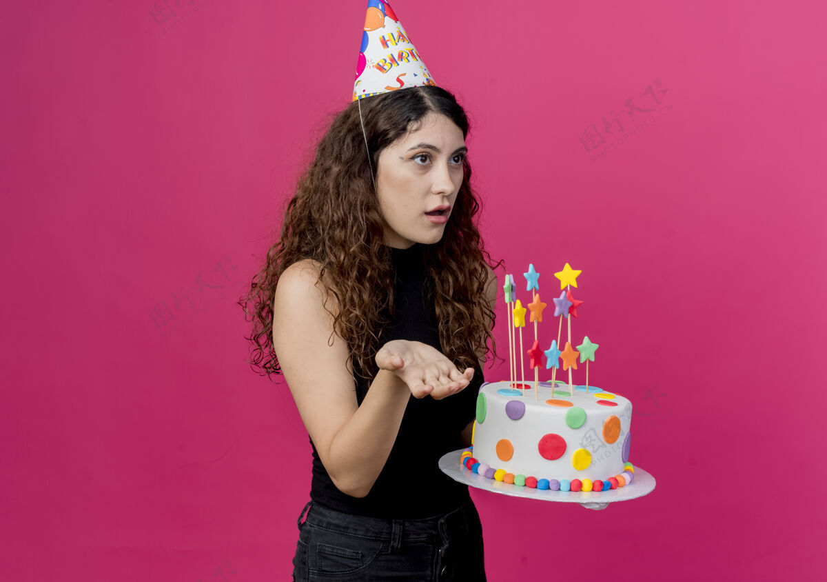 问一个年轻漂亮的女人 卷发 戴着节日帽 手里拿着生日蛋糕 一边困惑地看着一边 一边伸出手臂 一边问生日派对的概念蛋糕困惑抱着