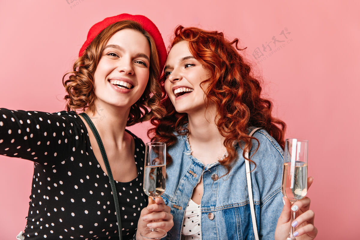 粉色背景两个迷人的女孩拿着酒杯自拍愉快的一些女士享受香槟和表达积极的情绪两个人女孩女人