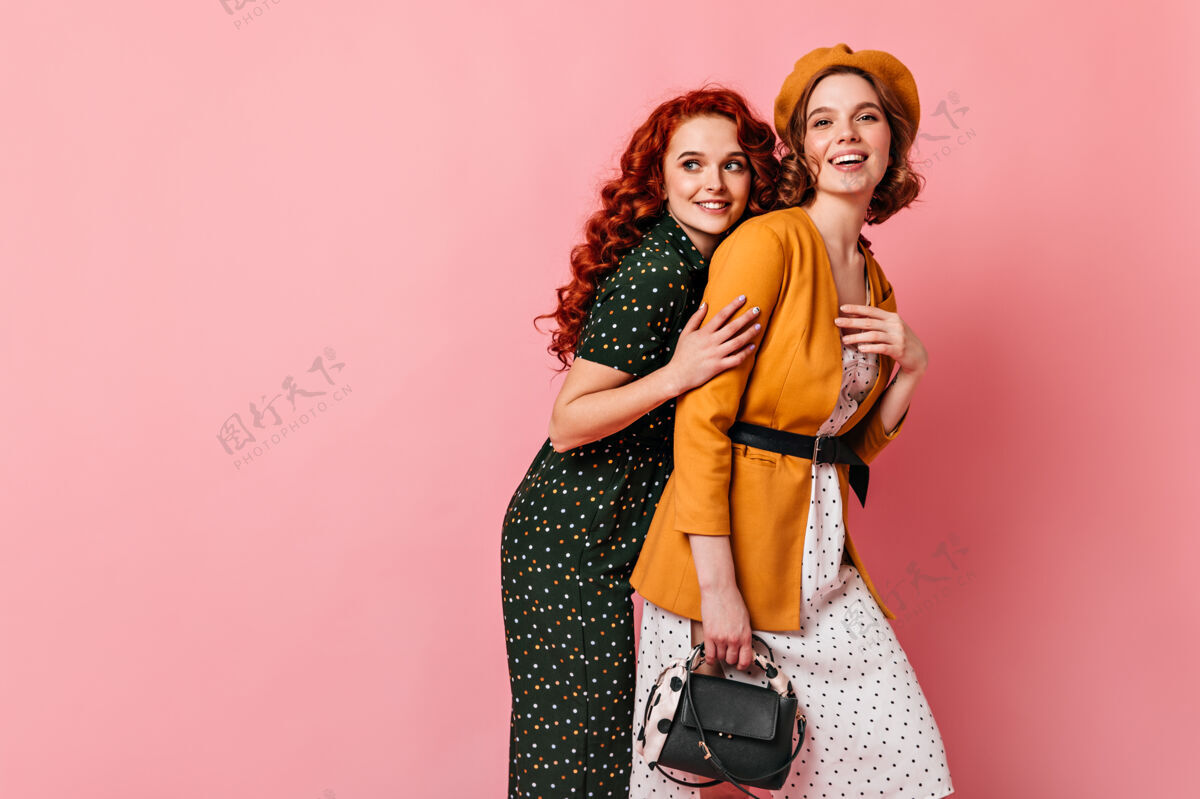 贝雷帽穿着贝雷帽的时髦女人和朋友拥抱在一起两个优雅的女孩在粉色背景下合影姜红发时尚