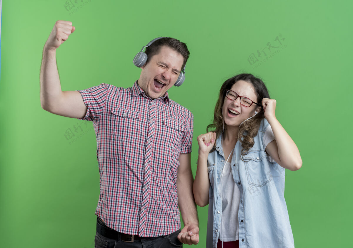 情侣一对年轻夫妇穿着休闲服 戴着耳机 快乐而兴奋地享受着喜爱的绿色音乐女人衣服绿色