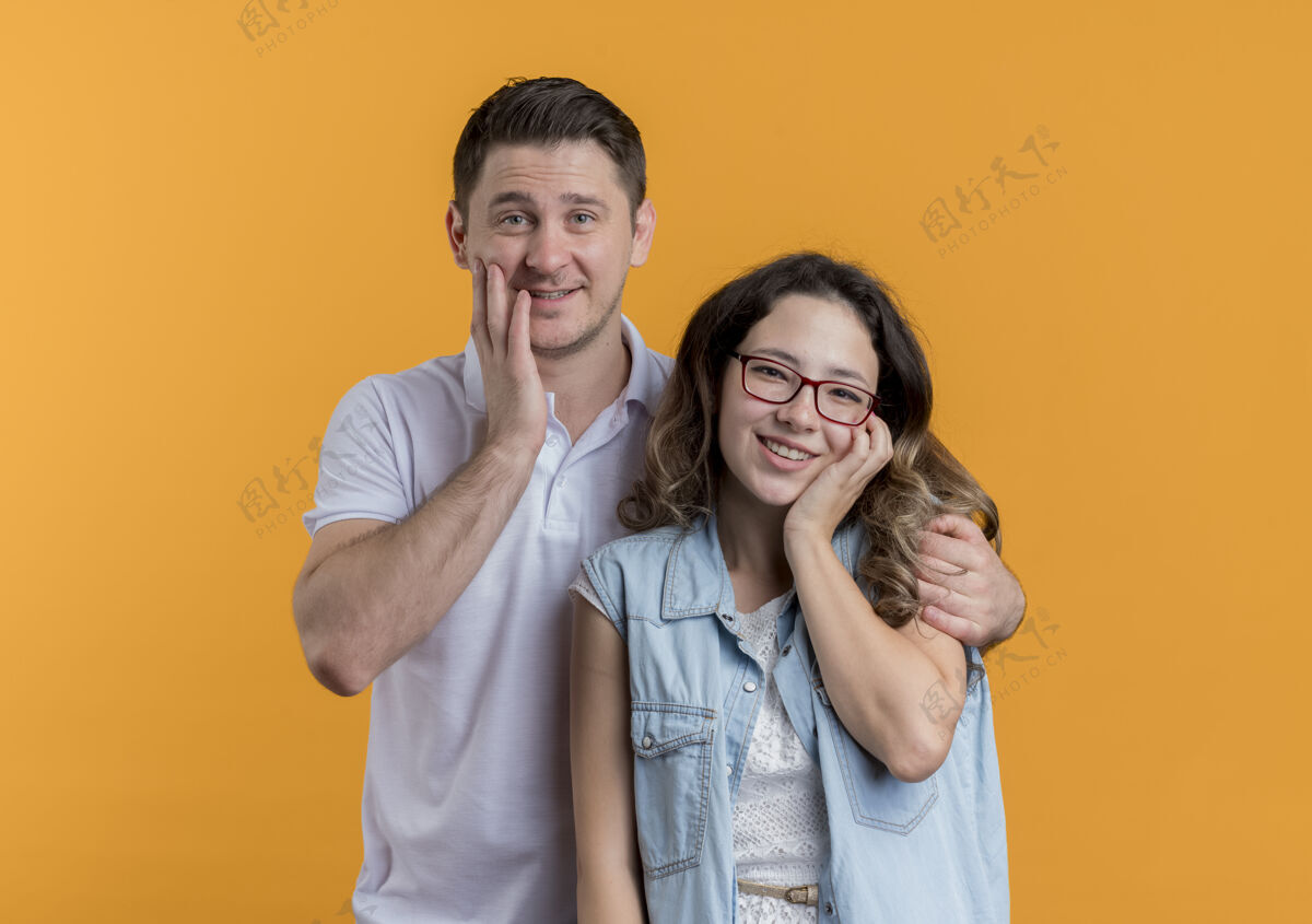 女人一对穿着休闲服的年轻夫妇幸福而积极地微笑着越过橘子休闲橙色快乐