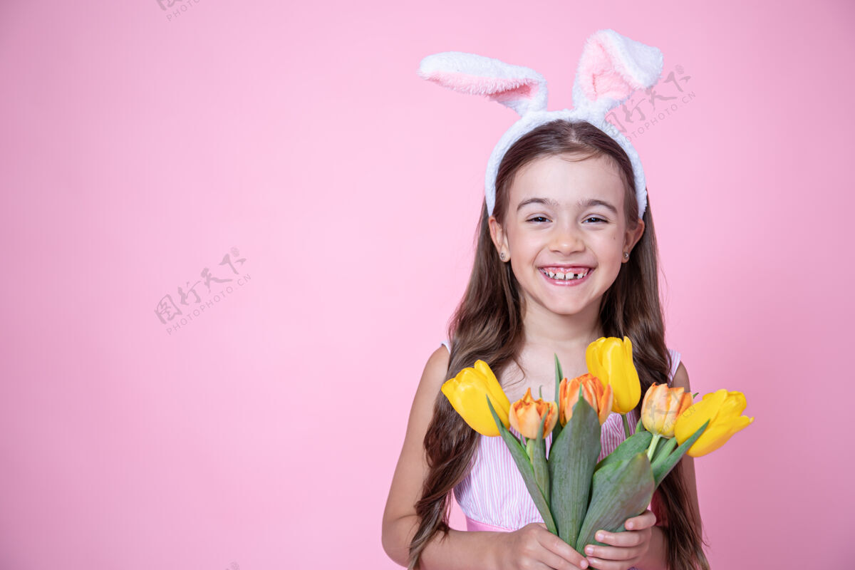 耳朵一个快乐的小女孩 带着复活节兔子耳朵 微笑着 手里拿着一束郁金香 站在粉色的画室里兔子兔子花