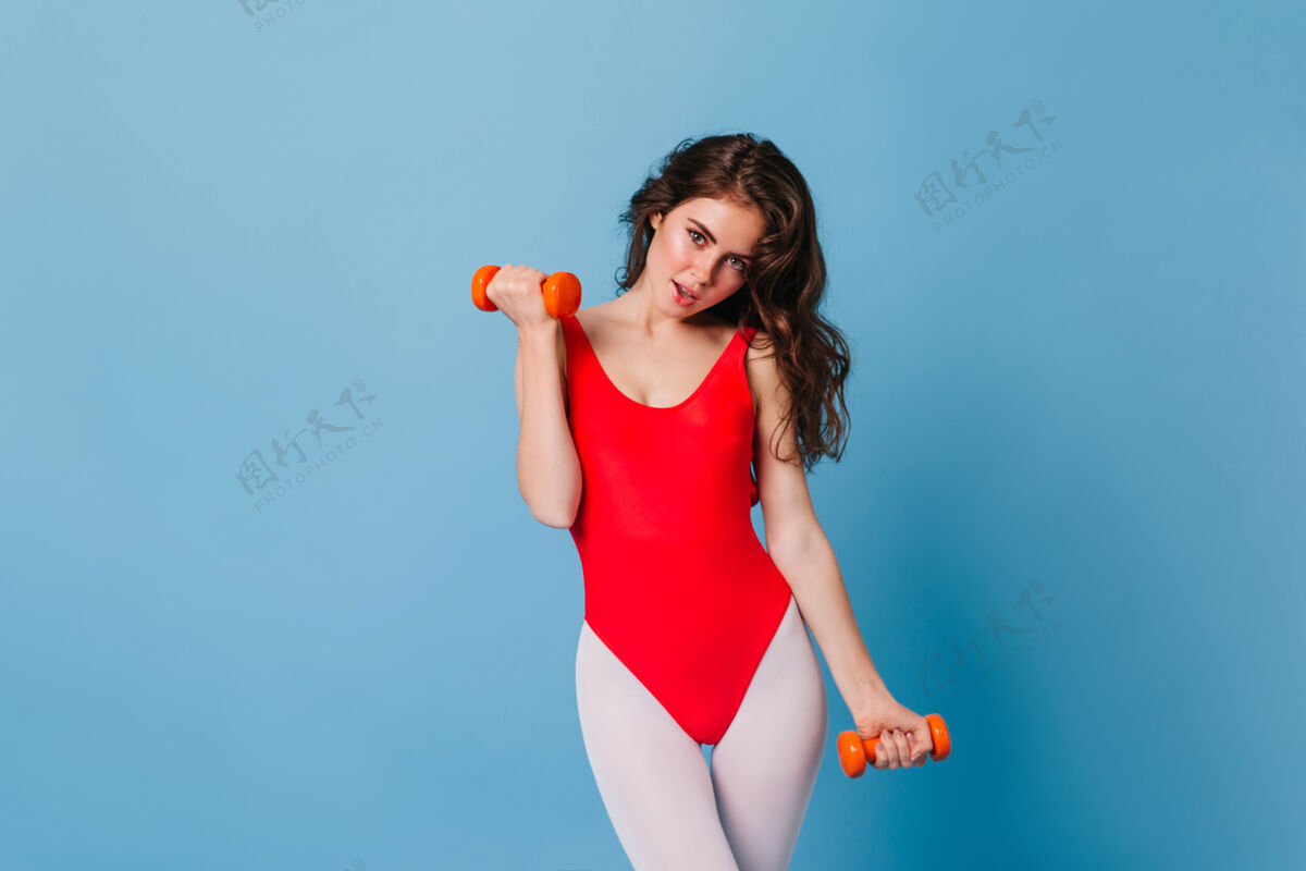 人穿着红色泳衣和紧身裤 做肱二头肌运动的迷人运动女性肖像理发锻炼健美操