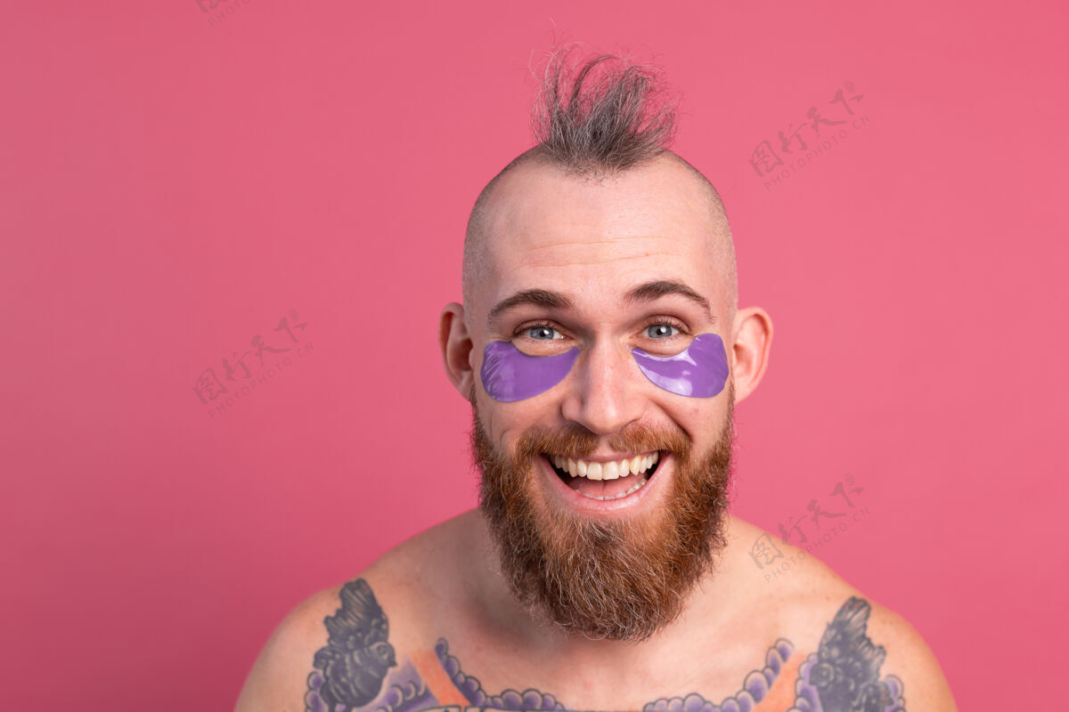 深色欧洲帅哥留着胡子纹身上身的男人戴着紫色眼罩对着镜头摆粉红色的姿势提升阳性化妆品