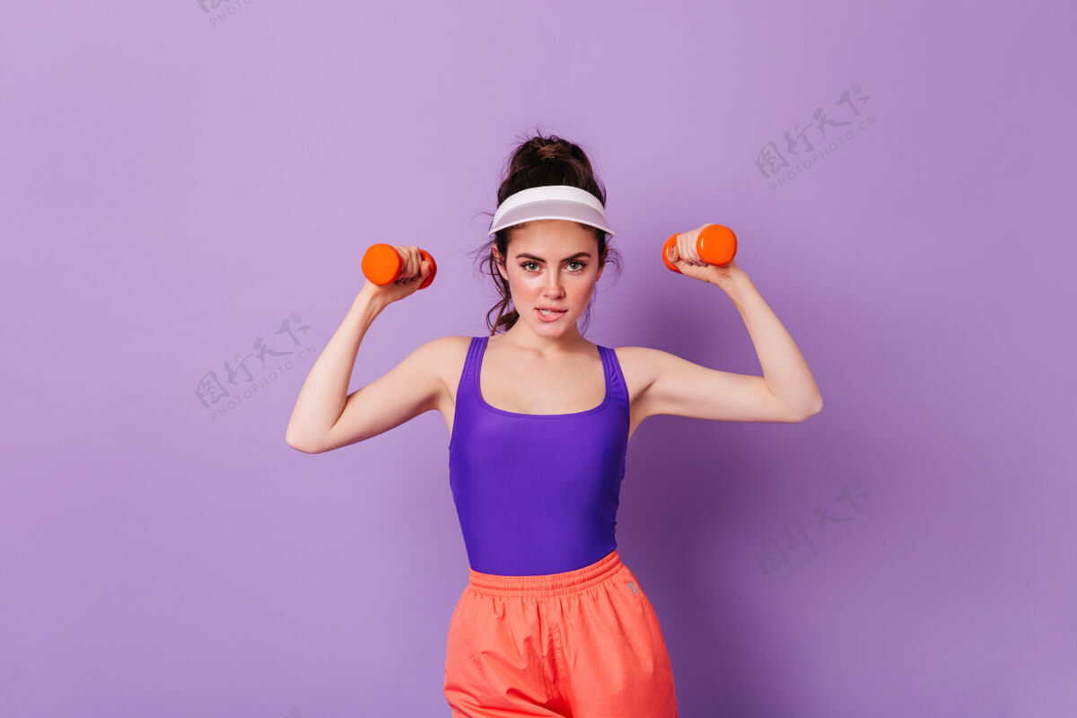 橙色裤子黑发女子用哑铃练习的画像紧身裤运动服健美操